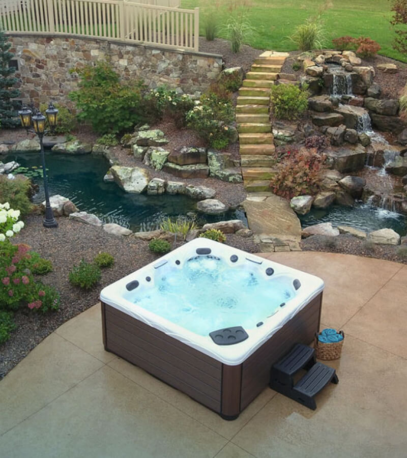 Stamped Concrete Patio with Hot Tub Landscape design features hot tub, stone garden, and flowing stream.